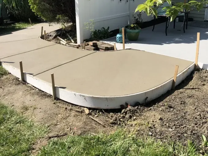 Curved concrete patio pad fresh in its forms with grade stakes set in a Cherry Hill, New Jersey back yard