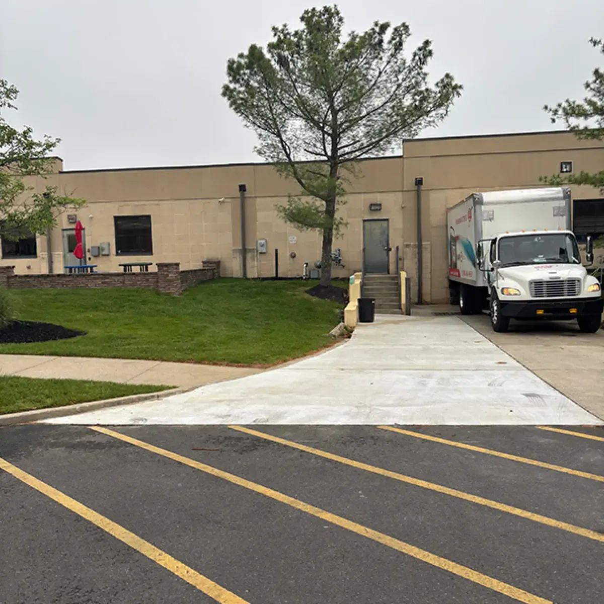 New concrete apron at the entrance of a commercial building parking lot with a box truck at the loading door