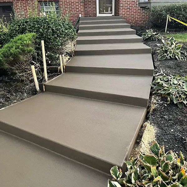 Wide new concrete steps climbing through a landscaped front yard to a brick home, like entries found in Osage, NJ
