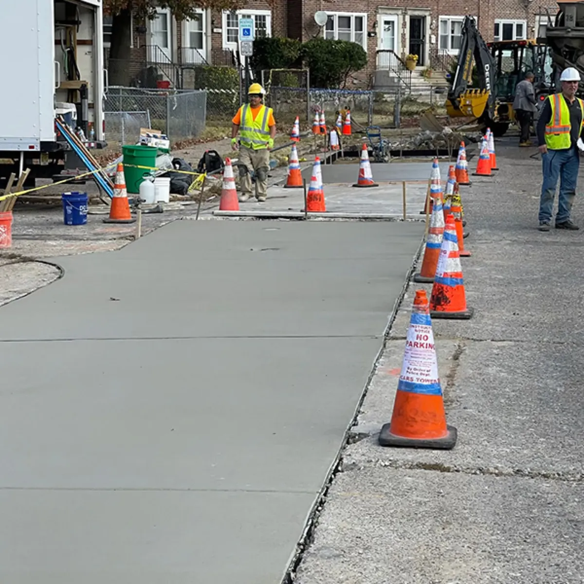 Crew placing new concrete in a long street repair section lined with orange traffic cones