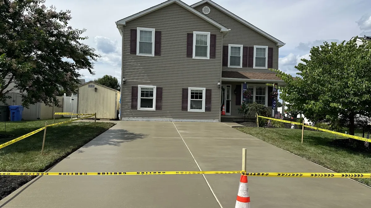 New gray concrete driveway poured to a two-story home, taped off while the slab sets