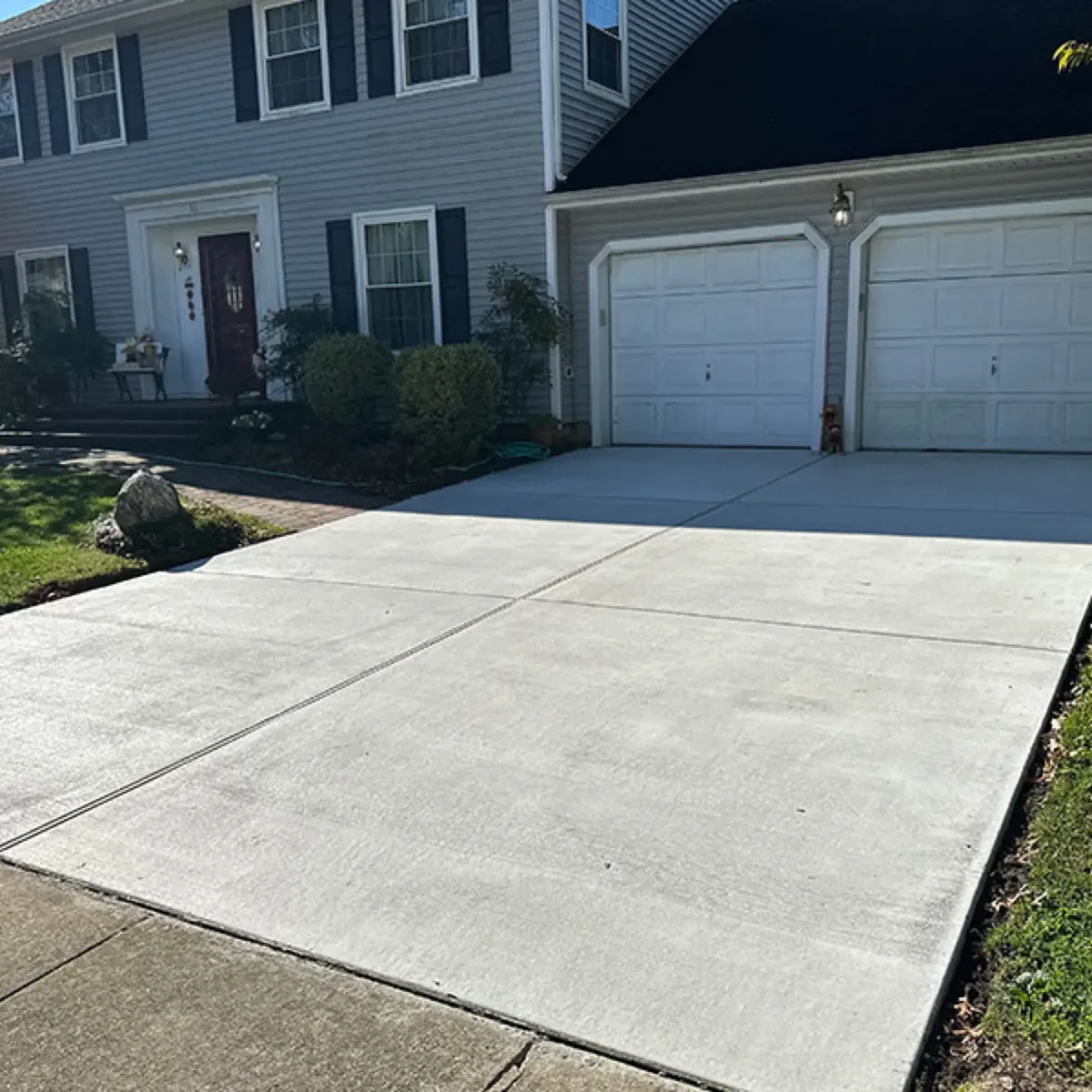 Finished concrete driveway running to a two-car garage at a suburban home, with cut control joints down the slab