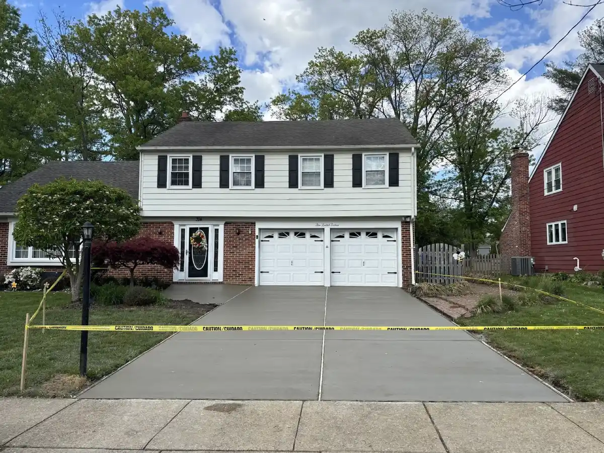 New concrete driveway curing behind caution tape at a brick colonial home with a two-car garage