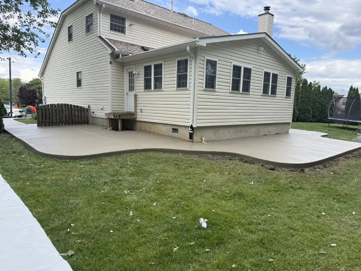 Large curved concrete patio poured behind a two-story colonial home, edged against the back lawn