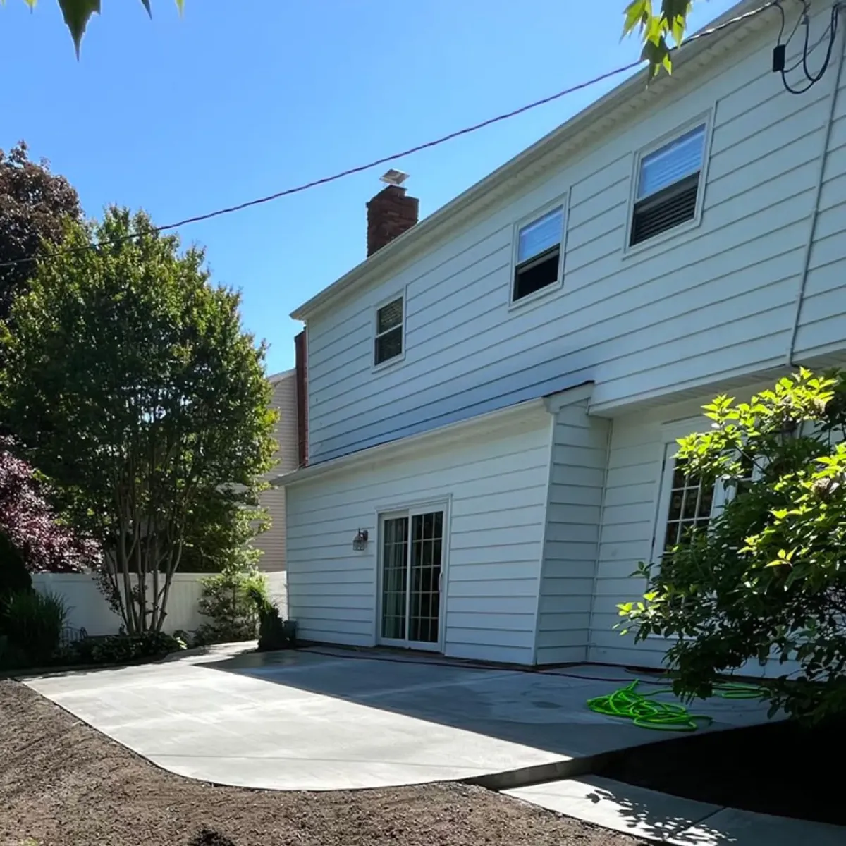 Finished light gray concrete patio slab spanning the back of a two-story home with lawn on both sides