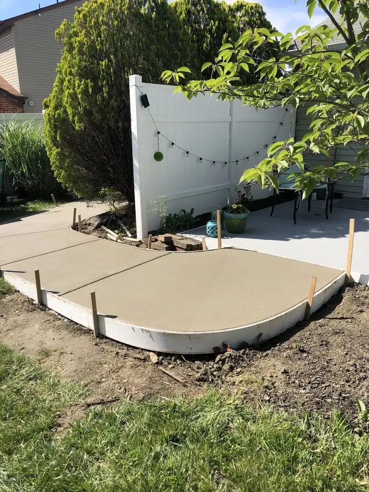 Freshly poured curved concrete patio pad still held in wood forms with stakes along the edge