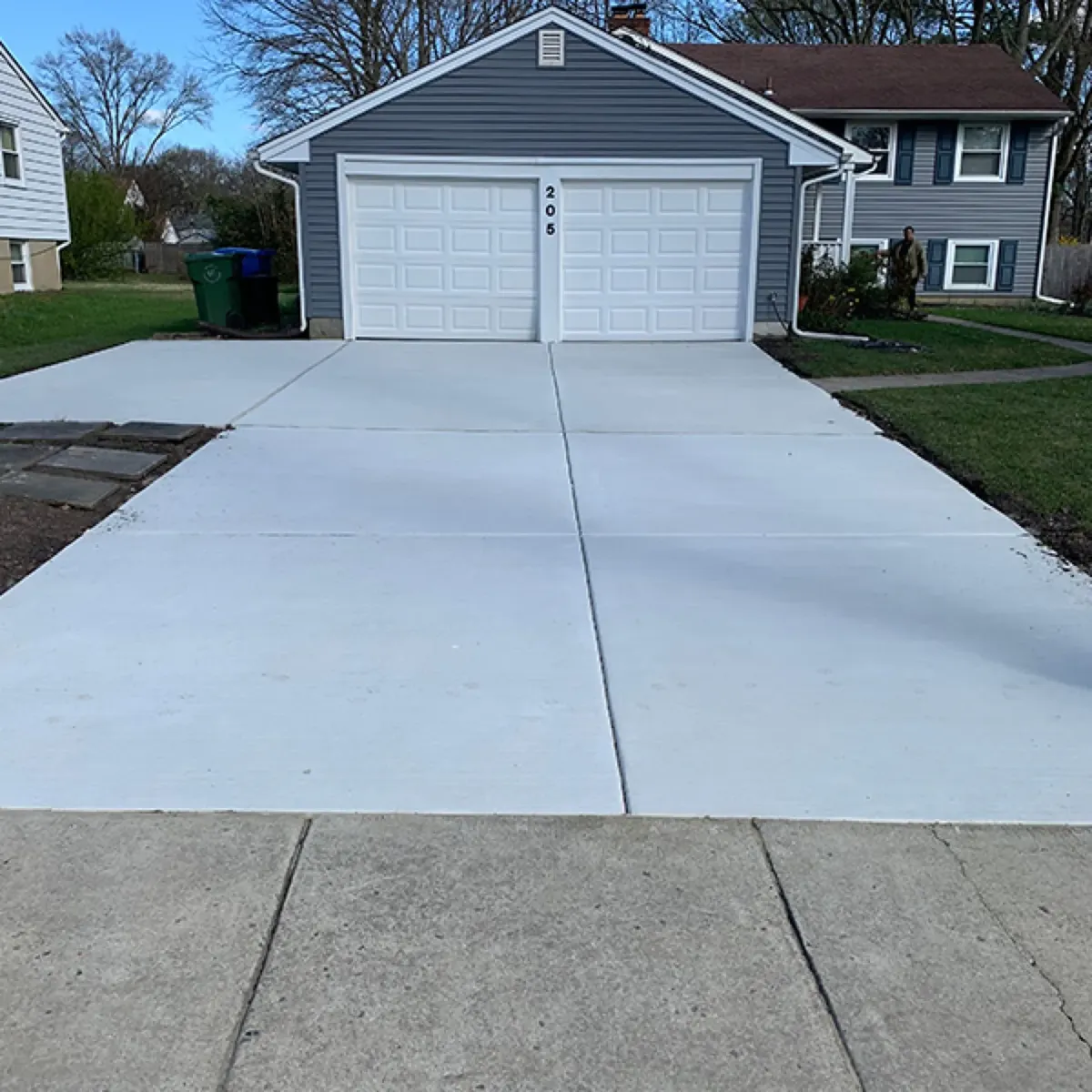 Finished light gray concrete driveway leading to a two-car garage with trimmed lawn edges on both sides