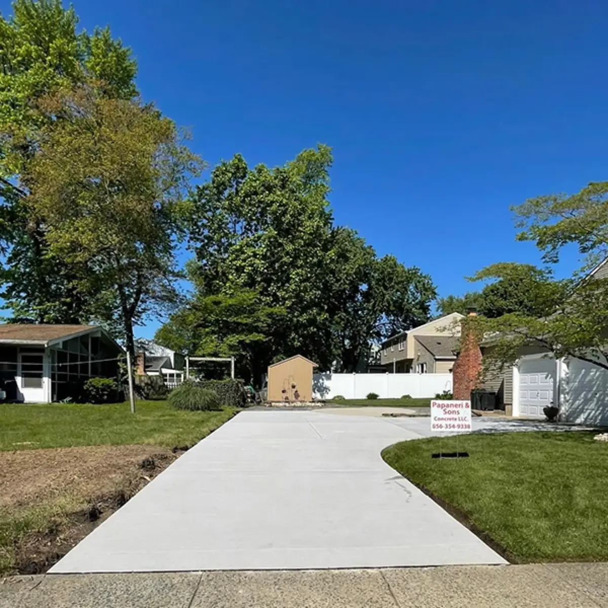 Long straight concrete driveway running from the street toward a single-story home under a clear sky