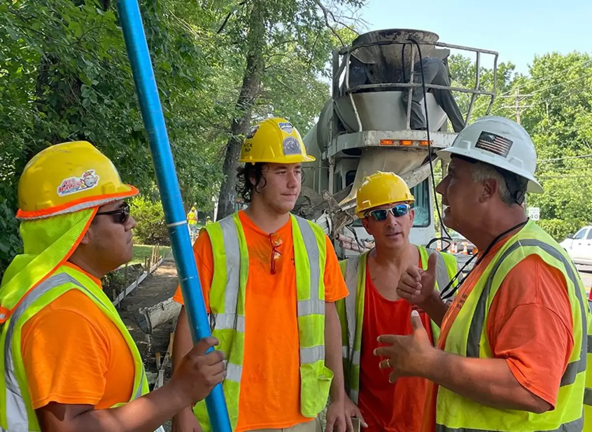Concrete crew in hard hats and safety vests talking beside a ready-mix truck on an active job site