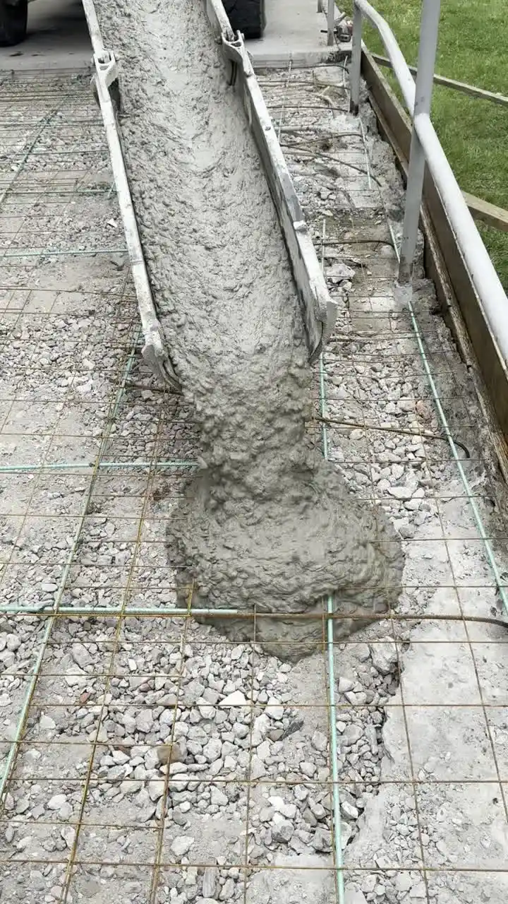 Fresh concrete sliding down a mixer chute onto compacted stone and wire mesh inside formed edges